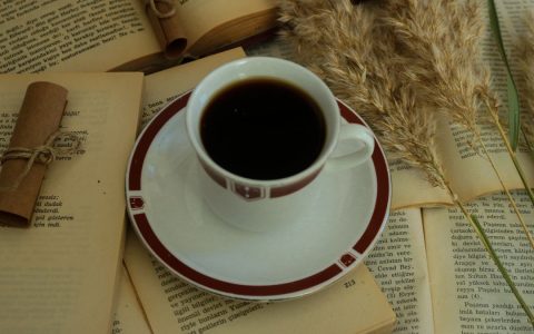 Cup of coffee surrounded by open books and dried flowers, conveying a cozy and educational vibe.