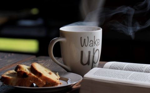 Steaming coffee with bread and an open book on a wooden table for a cozy morning.