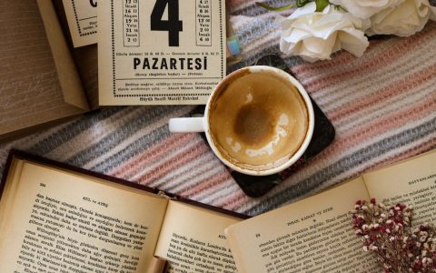 A cozy flat lay featuring coffee, open books, and flowers on a striped blanket.