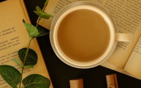 Warm still life featuring coffee, open books, and a sprig of greenery.