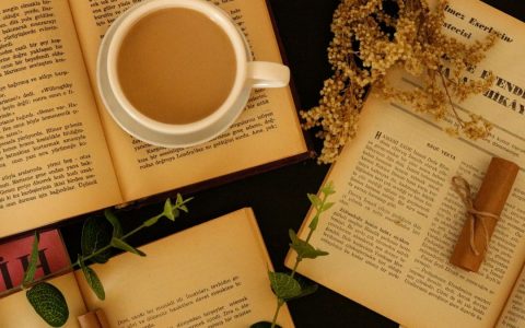 Flat lay of a coffee cup with open books and dried flowers for a cozy reading ambiance.