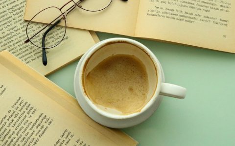 An inviting scene with a cup of coffee, open books, and eyeglasses for a cozy reading session.