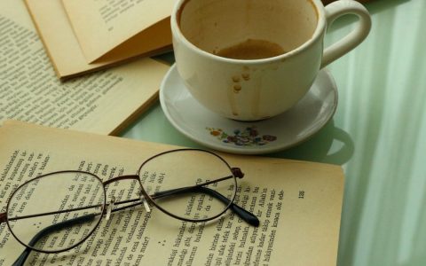 A warm and inviting setup featuring books, a cup of coffee, and eyeglasses on a glass table.