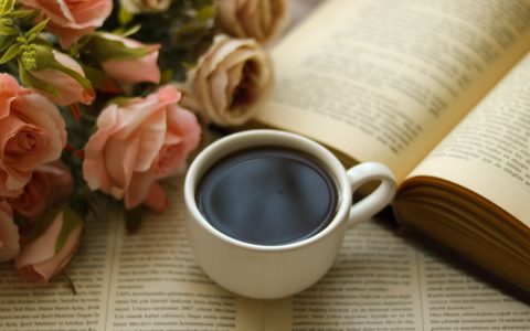 A serene still life featuring a coffee cup, open books, and blooming roses.