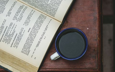 Top view of an open book and a cup of coffee on a wooden table, perfect for literature and coffee lovers.