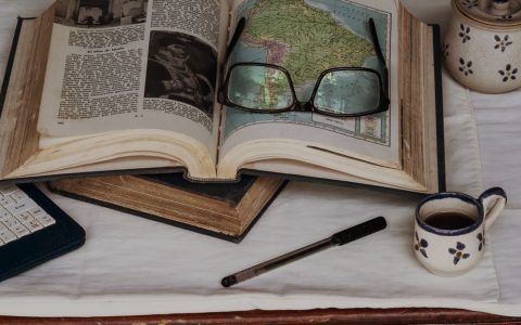 Explore and study with open book, maps, coffee, and glasses, perfect for a quiet afternoon.