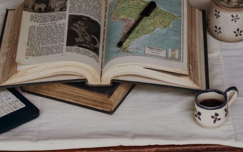 An open vintage book showing a map of South America, accompanied by a pen and a cup of coffee, evoking a scholarly atmosphere.