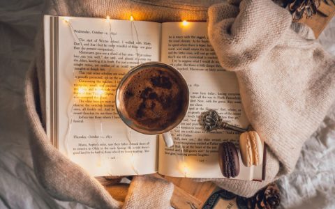 Warm and cozy setup with coffee, open book, sweater, and macarons for a relaxing autumn day.