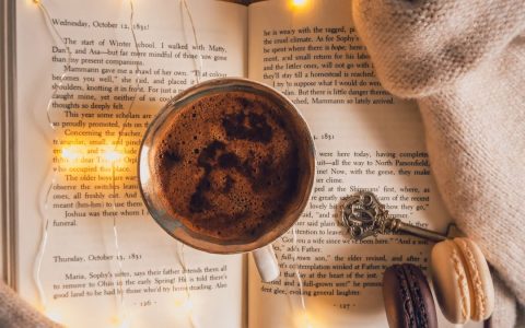 Warm coffee cup on an open book with macarons and fairy lights for a cozy reading ambiance.