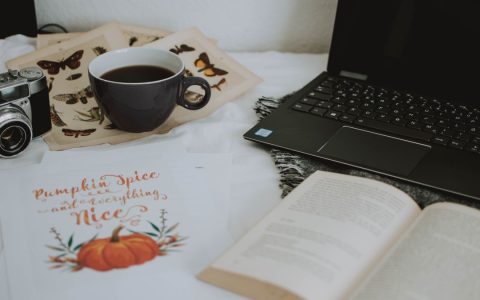 A cozy indoor workspace featuring a laptop, camera, coffee cup, and open books for a productive atmosphere.
