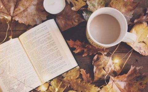 An inviting autumn scene with a book, warm drink, and glowing lights, perfect for a cozy day.