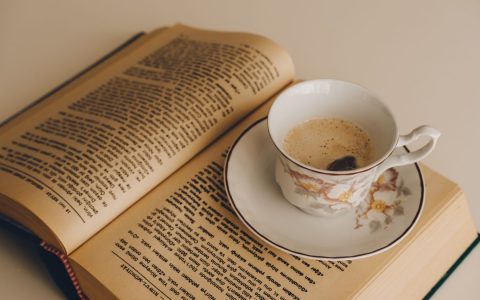 A porcelain cup with coffee placed on an open book, creating a cozy reading scene.