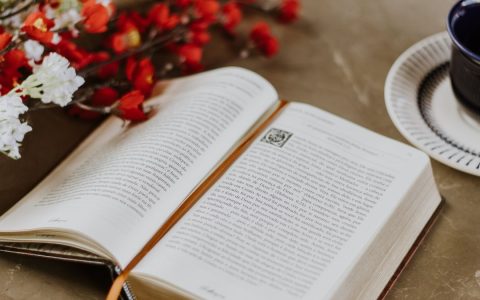 An open book with bright flowers and a coffee cup on a table, creating a cozy reading scene.