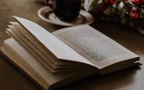 An open book lies on a table beside a coffee cup and flowers, offering a cozy reading ambiance.