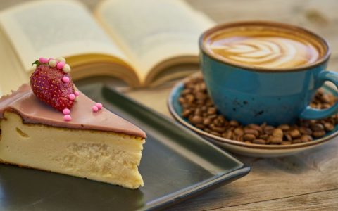 Slice of cheesecake and a latte on a table with an open book. Perfect for cozy moments.
