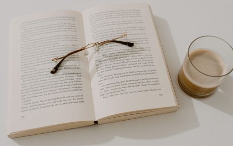 Open book with reading glasses and coffee on a white table, creating a serene reading corner.
