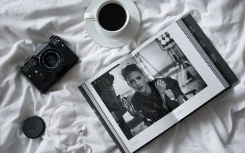 Artistic flat lay featuring a vintage camera, cup of coffee, and an open magazine on a bed.