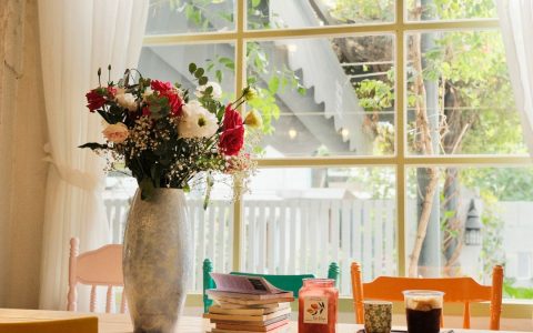 Cozy cafe table with flowers, books, and drinks by a bright window.