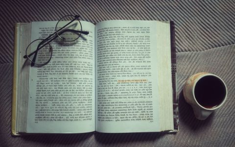 Open Hindi book with glasses and coffee cup on blanket, inviting cozy reading moment.