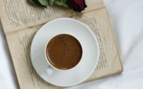 A steaming cup of coffee placed on an open book with a red rose on top, creating a cozy and romantic scene.