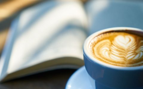 Warm latte art in a blue cup beside an open book, capturing a cozy morning vibe.