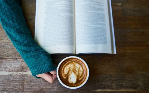 A cozy moment of reading a book with a latte art coffee in a warm café setting for relaxation.