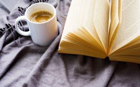 Warm coffee and an open book on a cozy blanket, perfect for a relaxing read.