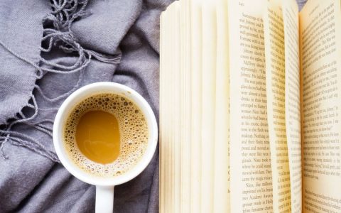A relaxed flatlay featuring an open book and a coffee mug on a cozy blanket, perfect for leisure moments.