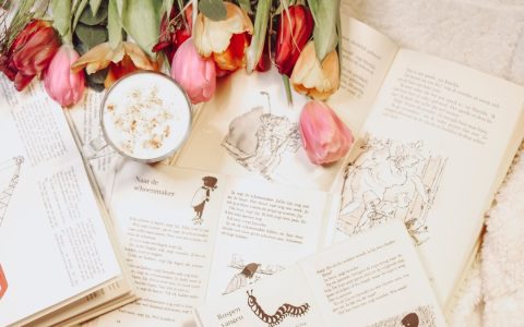 Aesthetic flat lay of open books, colorful tulips, and a cozy hot drink.
