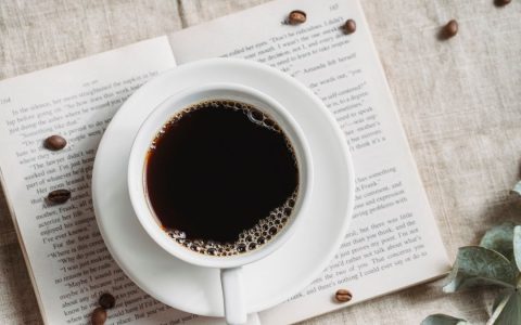A relaxing setup featuring a cup of black coffee on an open book with scattered coffee beans.