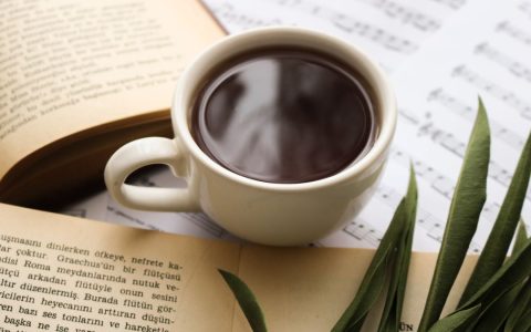 Cup of coffee with open books and music sheets, perfect for a cozy morning ambiance.