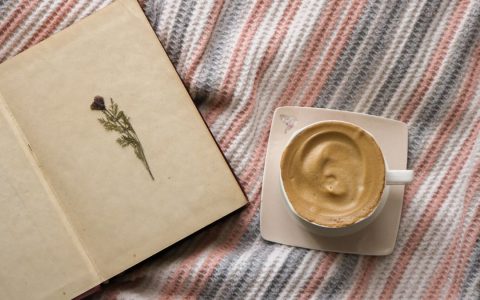 Coffee cup on a blanket with an open book. Perfect cozy setting for relaxation.