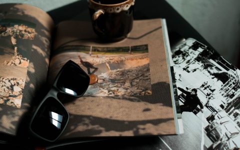 From above of trendy sunglasses and cup of drink placed on opened magazines with pictures on table
