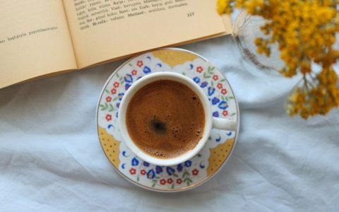 A cozy setup with a coffee cup, open book, and yellow flowers on a fabric background.