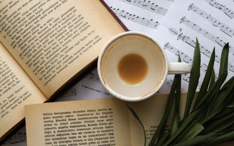 Top view of an empty coffee cup with books and sheet music creating a cozy and artistic atmosphere.