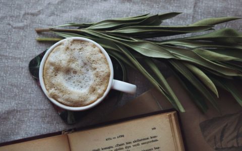 A warm cup of coffee with open book and leaves on a table, perfect for a cozy day.