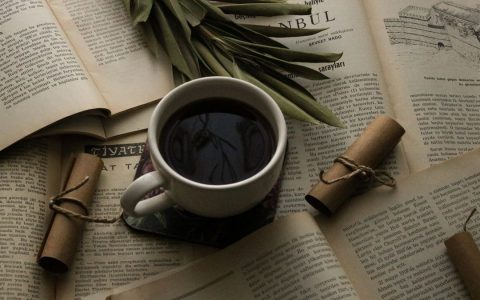 Warm flat lay featuring a coffee cup surrounded by open books and rolled paper scrolls.