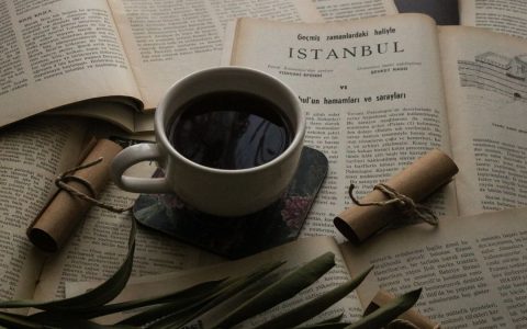A warm cup of coffee placed on an Istanbul-themed open book, surrounded by rolled papers and vintage pages.