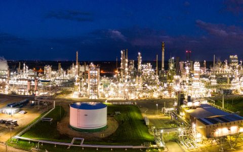 Aerial night view of a brightly lit industrial oil refinery with smoking chimneys in Rosemount, MN, USA.