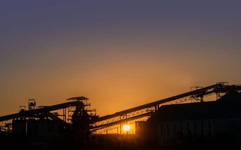 Silhouette of an industrial factory at sunset with a vibrant sky.