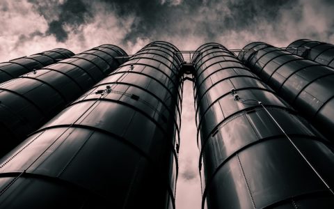Low angle view of industrial silos with a dramatic cloudy sky in the background, emphasizing modern industry.