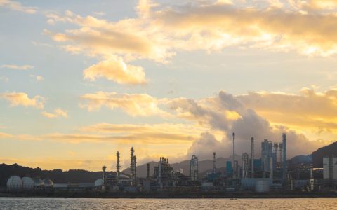 A stunning view of industrial chimneys and skyline with smoke at sunset over the water.