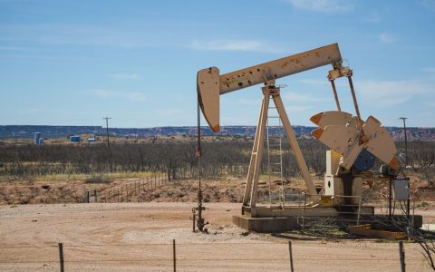 Industrial oil pumpjack in a desert setting under a clear blue sky, illustrating oil extraction technology.