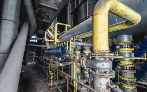 Close-up of an intricate industrial pipeline system featuring yellow valves and steel structures inside a factory.