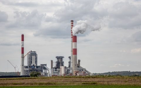 A scenic view of a power plant with smokestacks emitting smoke, set against a cloudy sky.