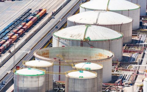 Aerial shot of large oil storage tanks in an industrial district with adjacent railway tracks.