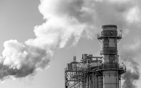 Monochrome image of industrial smokestack releasing steam into the sky.