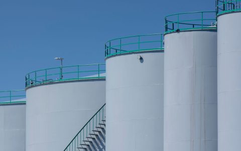 Large industrial storage tanks with green railings against a clear blue sky.
