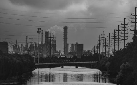 Moody black and white photo of an industrial river scene with power lines and factories.
