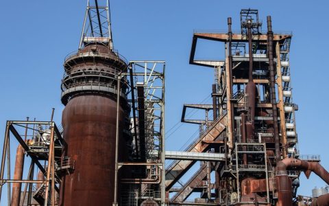 Close-up of a large rusted industrial metal structure with blue sky background.